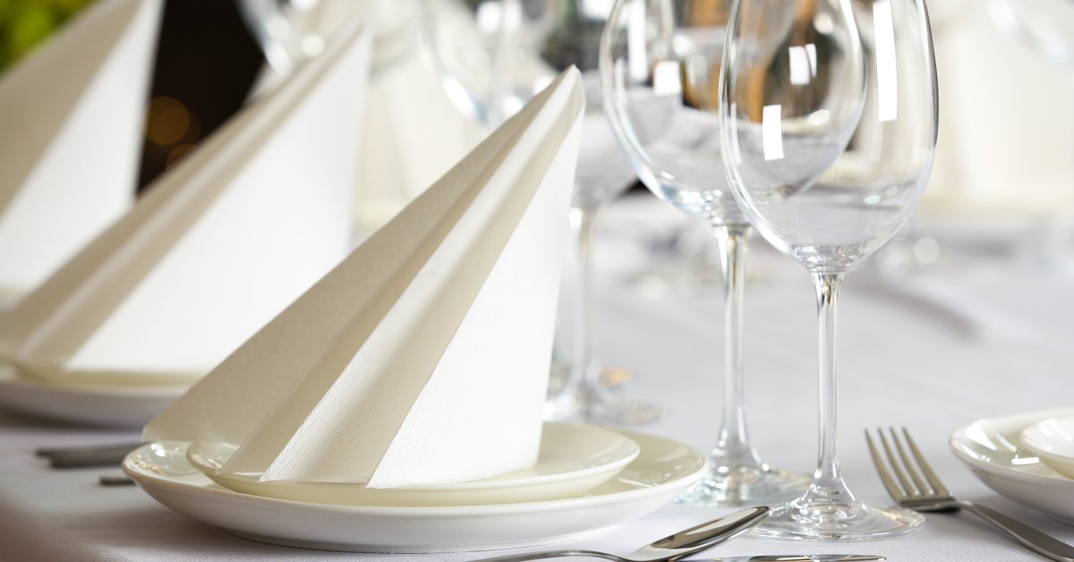 A fancy place setting on a table. Two wine glasses, a silverware set, and a folded napkin are on the table.