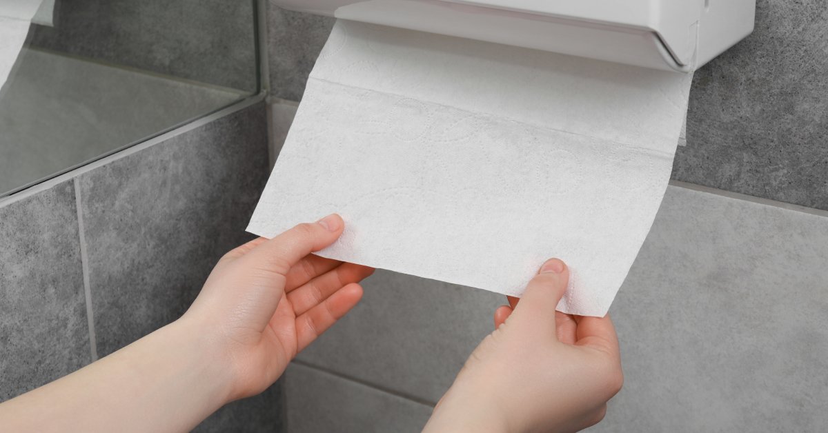 A woman's hands next to a mirror in a public bathroom. She is grabbing and pulling down on a fresh paper towel.