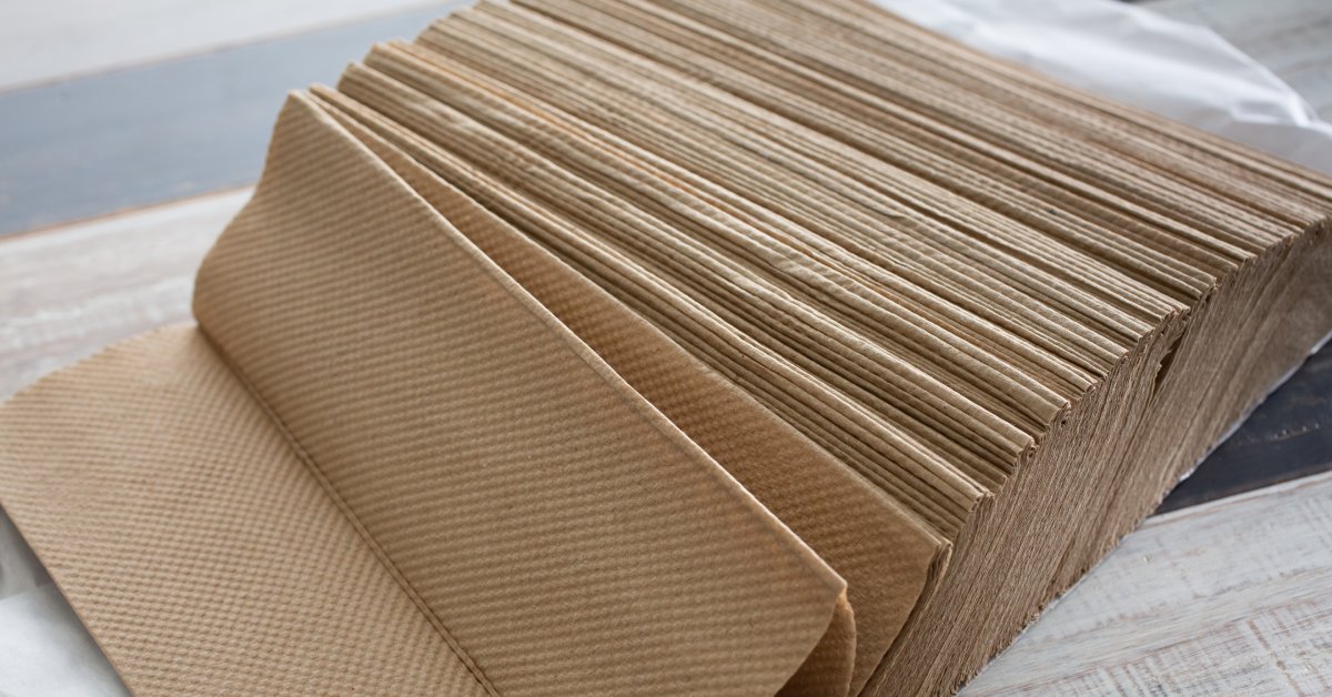 A large stack of recycled paper towels laying on its side. They are placed on a table and are falling to one side.