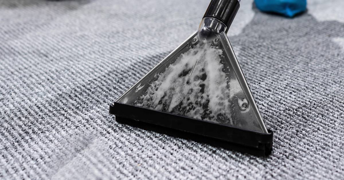 Close-up to the soapy plastic triangular head of a large cleaning extractor, cleaning a grey and white carpet.