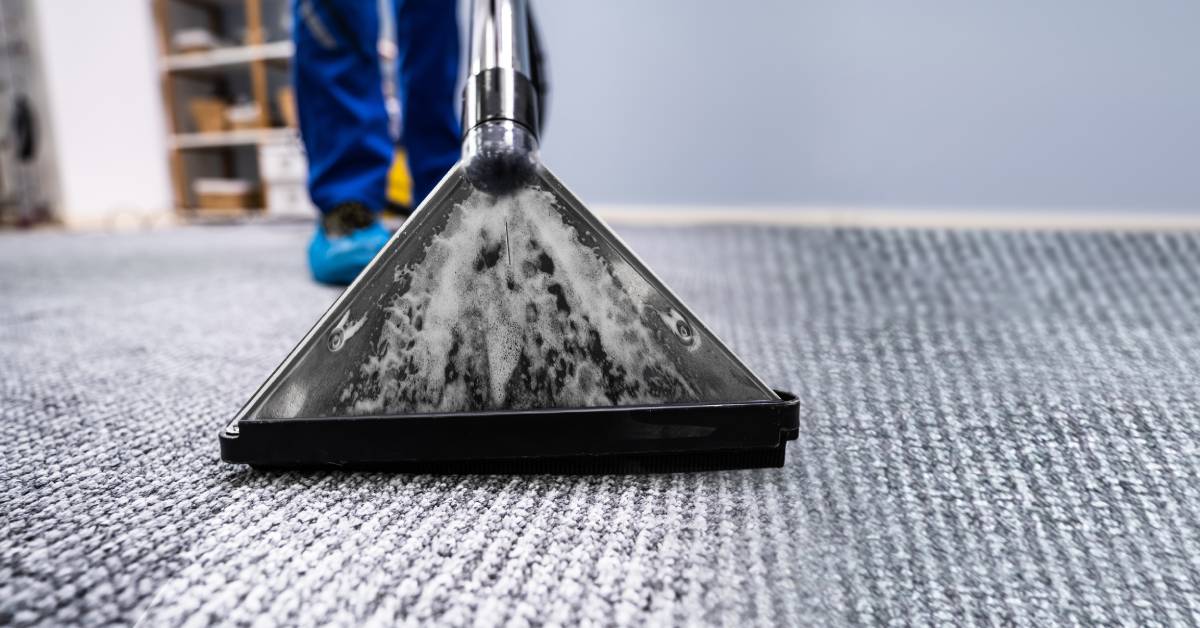 Close-up to the black plastic triangular head of an extractor leaving a clean trail on a carpet with two legs in background.