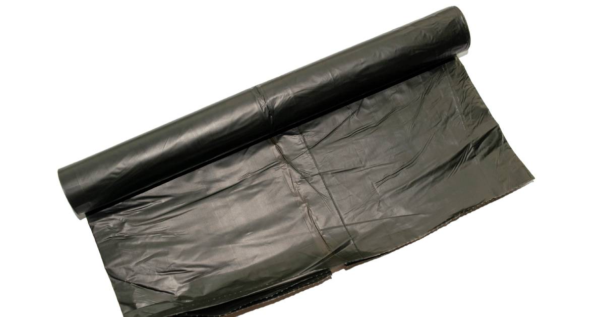 A wide roll of thick black plastic trash bags with wrinkles is unrolling in front of a white background.