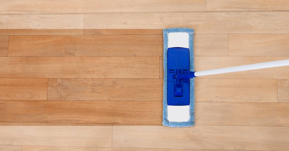 An overhead view of a wooden floor with a blue mop running across the middle, leaving a wide clean line.