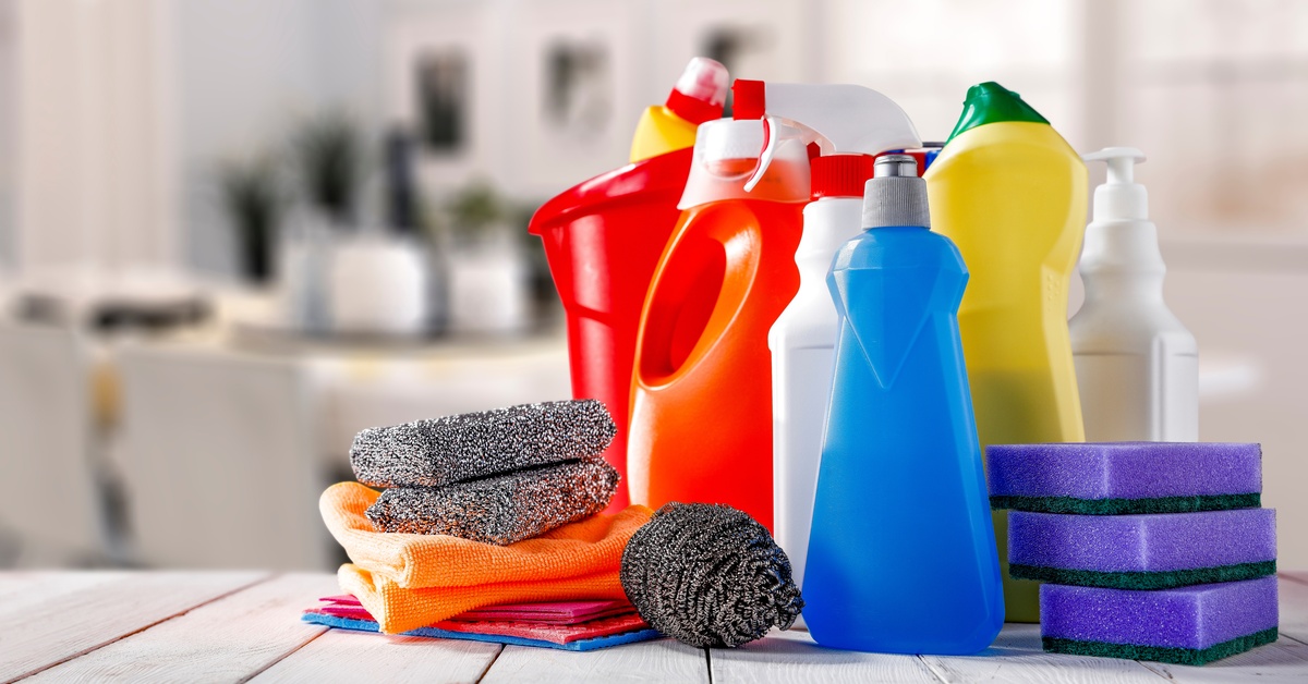Multiple plastic bottles of different sizes and shapes with multiple sponges and cloths placed on a wooden surface.