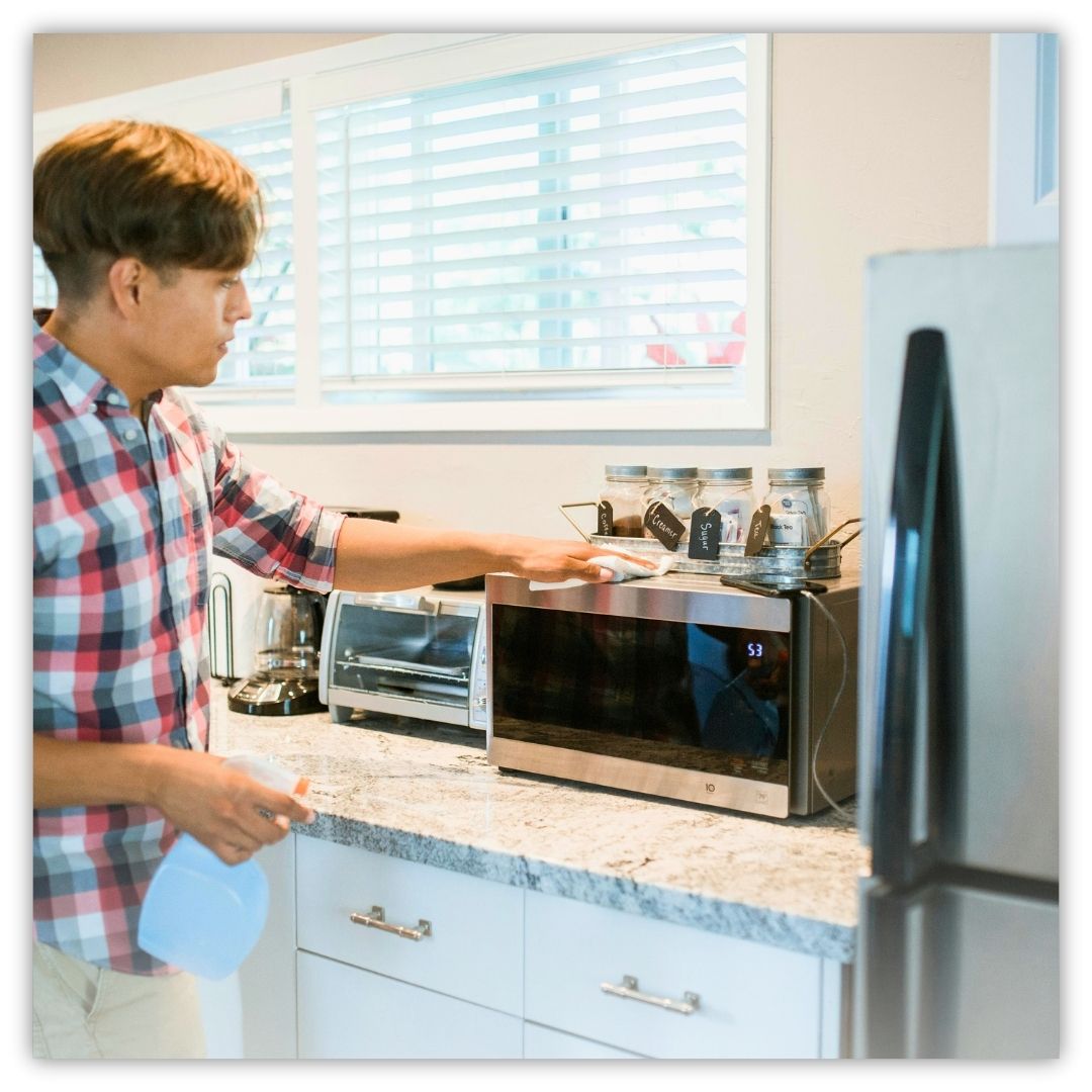 a man cleaning the exterior of a microwave