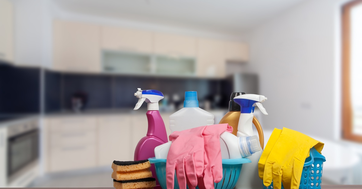 Multiple bottles of cleaning supplies, latex gloves, and sponges, on top of a counter inside of a large kitchen.
